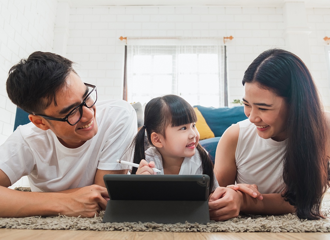 Service Your Policy - Happy Mother and Father Laugh With Their Daughter as She Uses a Tablet at Home